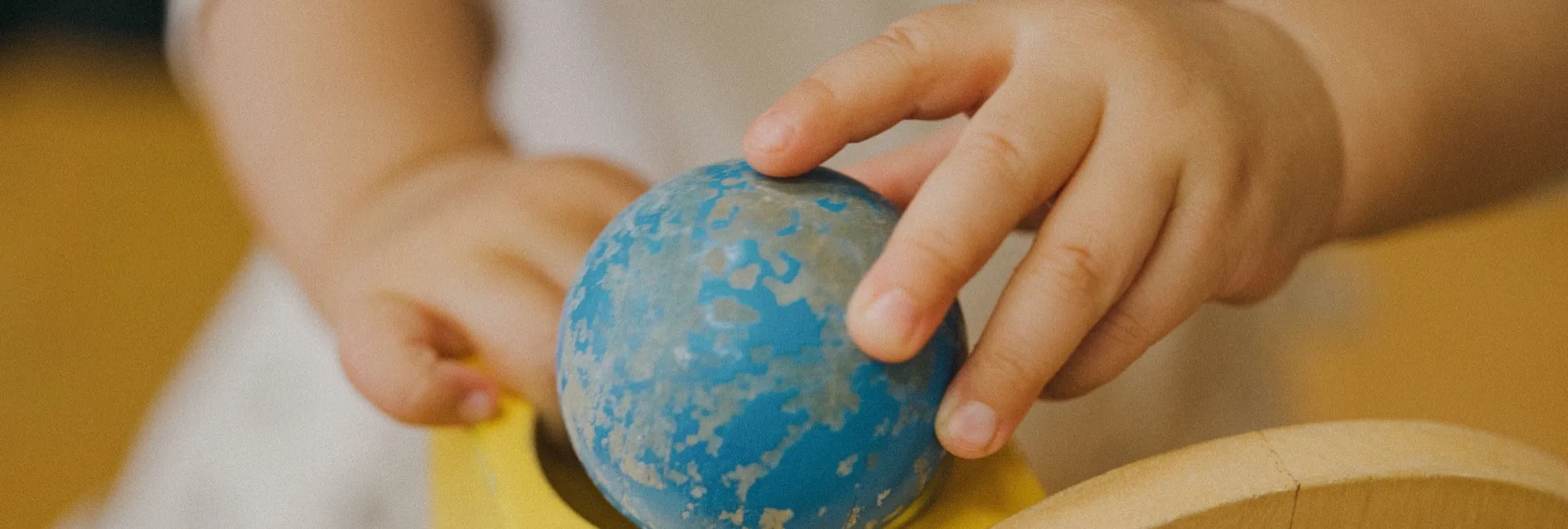 Kinderhandjes spelen met een blauwe bal en houten speelgoed